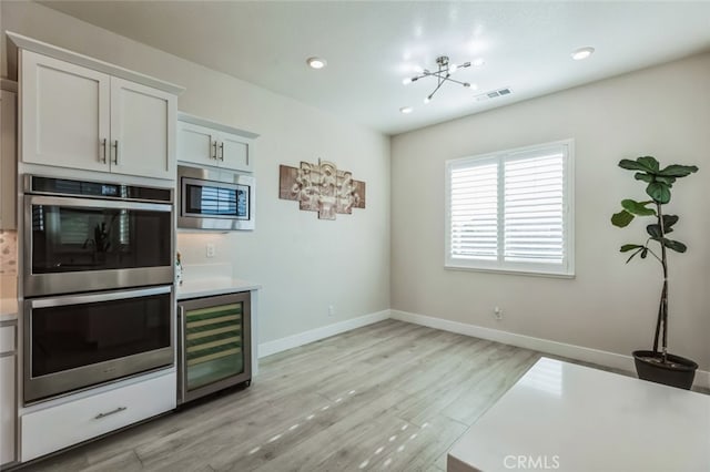 kitchen featuring white cabinetry, stainless steel appliances, light wood-type flooring, and wine cooler