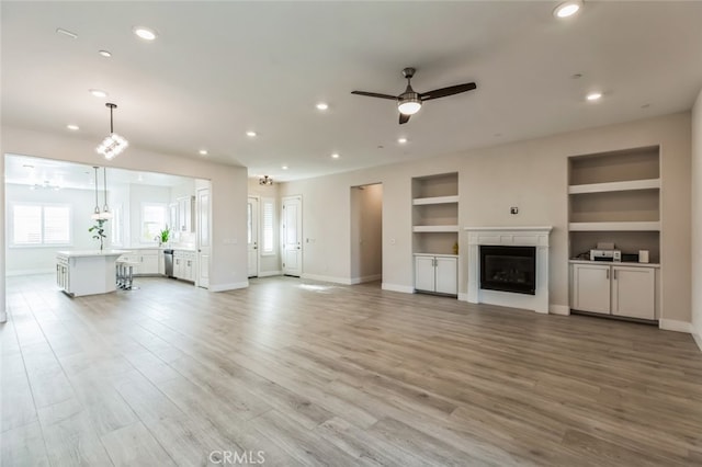 unfurnished living room featuring ceiling fan, built in features, and light wood-type flooring