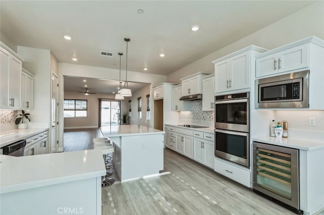 kitchen with stainless steel appliances, decorative backsplash, white cabinets, decorative light fixtures, and beverage cooler