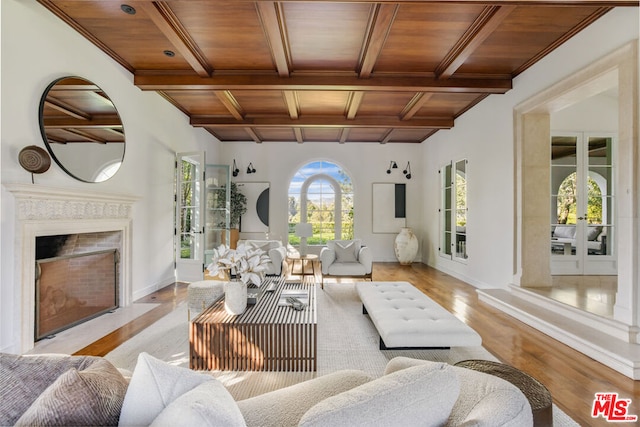 living room featuring wood ceiling, a high end fireplace, light hardwood / wood-style floors, french doors, and beamed ceiling