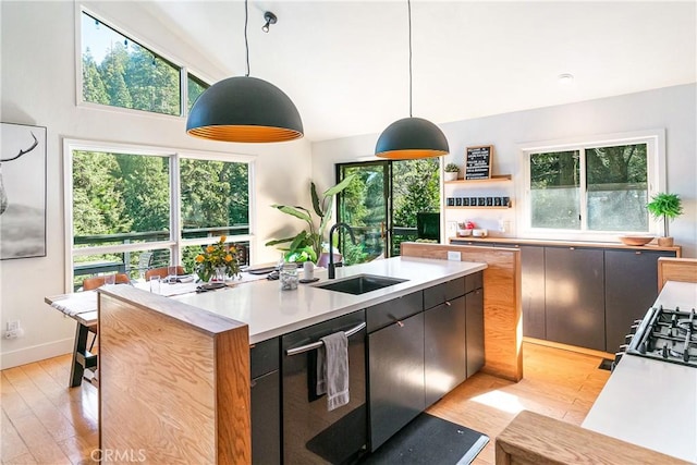 kitchen featuring pendant lighting, sink, stainless steel dishwasher, and light wood-type flooring