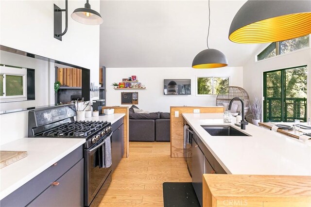 kitchen with hanging light fixtures, black gas stove, sink, and light hardwood / wood-style floors