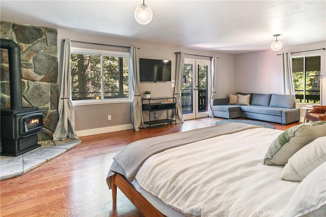 bedroom with multiple windows, access to outside, wood-type flooring, and a wood stove