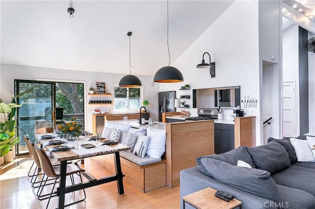 kitchen featuring refrigerator with ice dispenser, stainless steel stove, hanging light fixtures, high vaulted ceiling, and light hardwood / wood-style floors