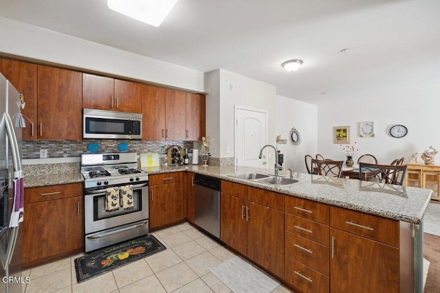 kitchen featuring sink, tasteful backsplash, appliances with stainless steel finishes, kitchen peninsula, and light stone countertops