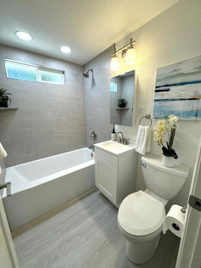 full bathroom featuring toilet, wood-type flooring, a textured ceiling, vanity, and tiled shower / bath combo