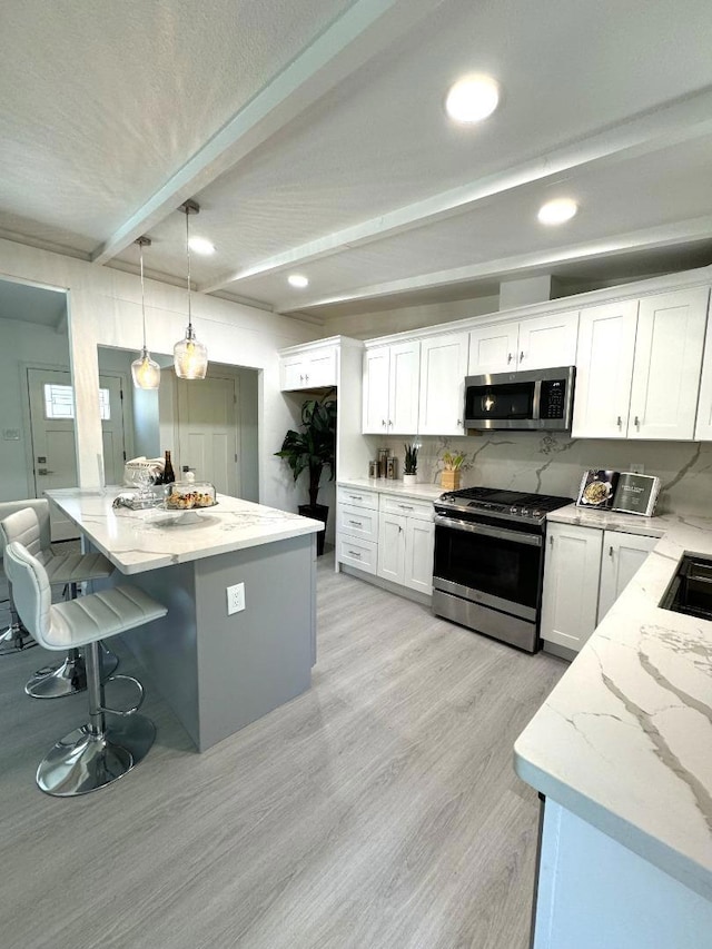 kitchen with appliances with stainless steel finishes, pendant lighting, white cabinetry, light stone countertops, and beam ceiling