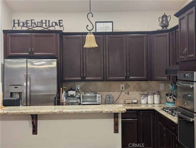 kitchen with hanging light fixtures, dark brown cabinets, stainless steel appliances, light stone counters, and decorative backsplash