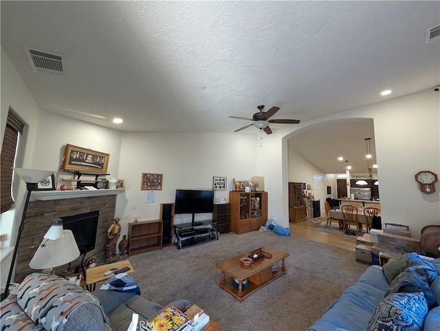 living room featuring ceiling fan, a stone fireplace, carpet floors, and a textured ceiling