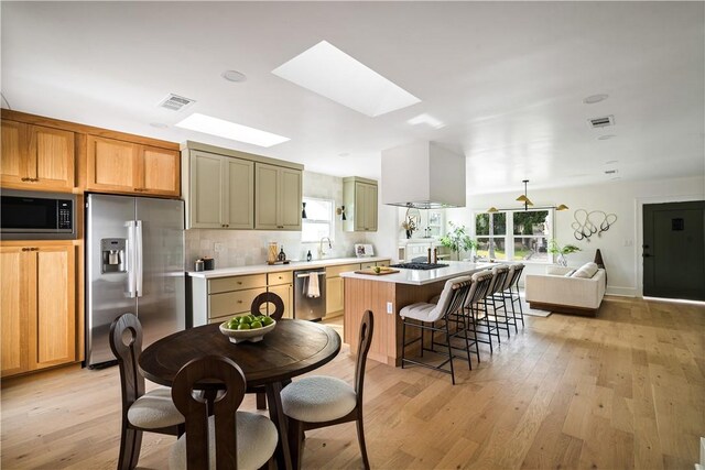 kitchen with appliances with stainless steel finishes, a skylight, tasteful backsplash, range hood, and light wood-type flooring