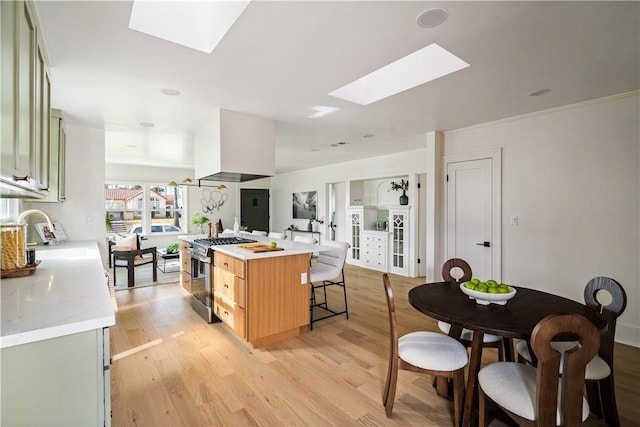 kitchen featuring sink, stainless steel gas stove, a skylight, a center island, and exhaust hood