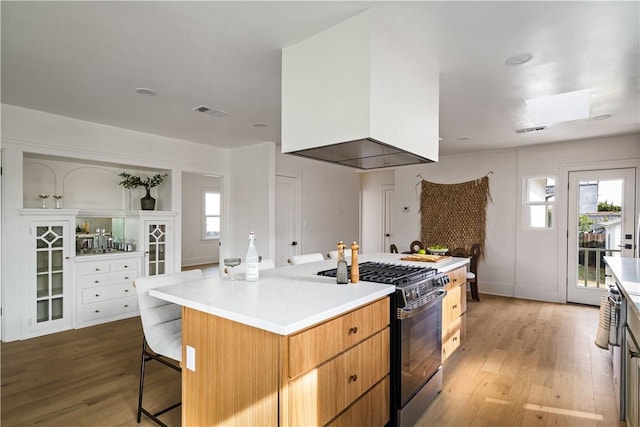 kitchen with a kitchen island, range with gas stovetop, light hardwood / wood-style floors, a kitchen bar, and exhaust hood