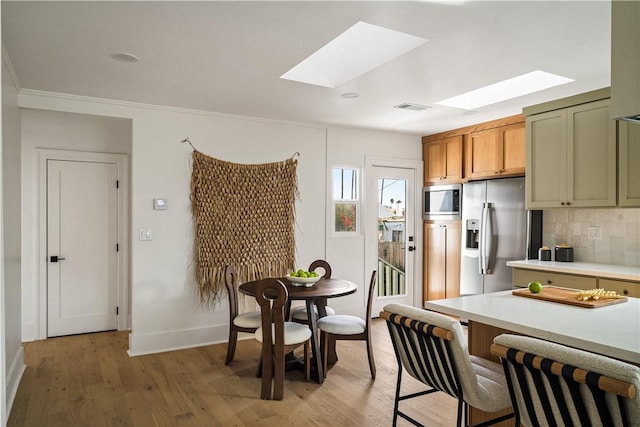 kitchen with appliances with stainless steel finishes, a skylight, backsplash, green cabinetry, and light wood-type flooring