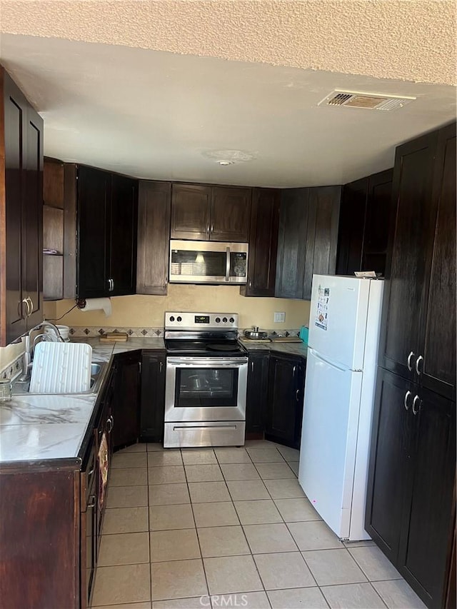 kitchen with dark brown cabinetry, appliances with stainless steel finishes, sink, and light tile patterned floors