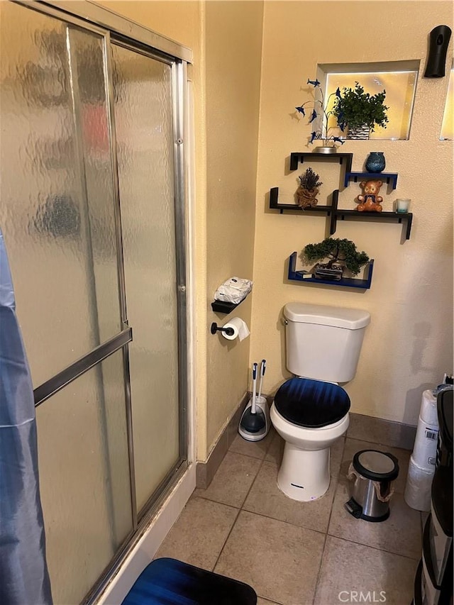 bathroom featuring tile patterned floors, toilet, and a shower with door