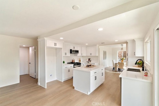 kitchen featuring sink, light hardwood / wood-style flooring, a kitchen island, gas range oven, and white cabinets