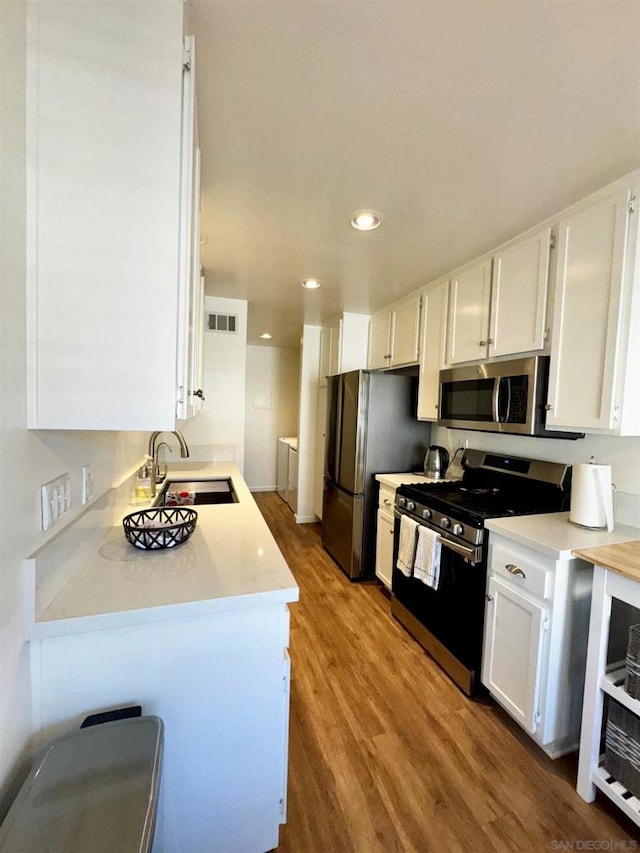 kitchen featuring washing machine and clothes dryer, stainless steel appliances, sink, and white cabinets