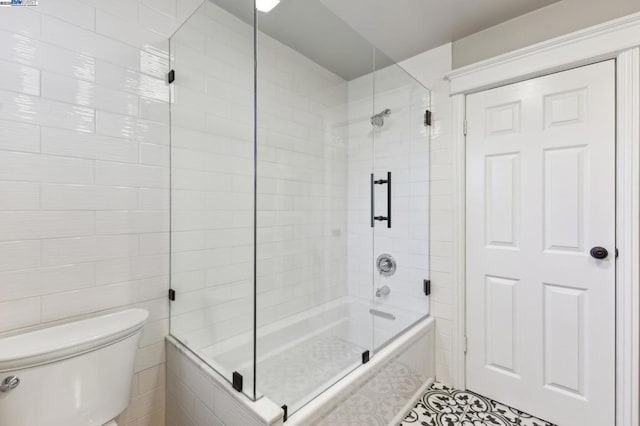 bathroom with tile patterned flooring, bath / shower combo with glass door, tile walls, and toilet