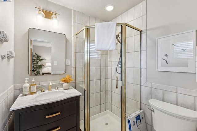 bathroom featuring vanity, a shower with shower door, tile walls, and toilet