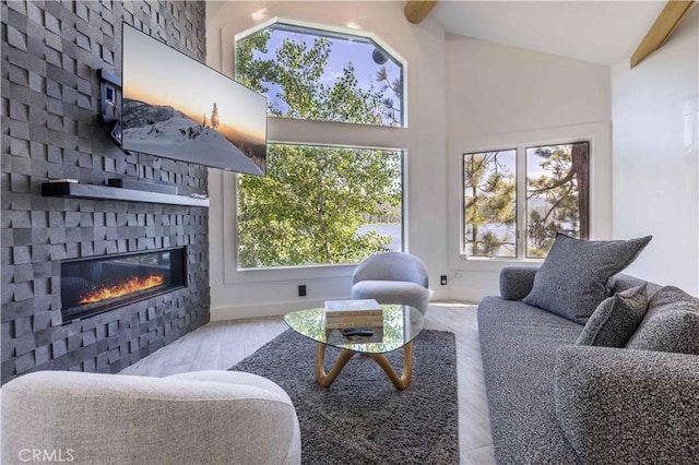 living room featuring beamed ceiling, a fireplace, light wood-type flooring, and a wealth of natural light