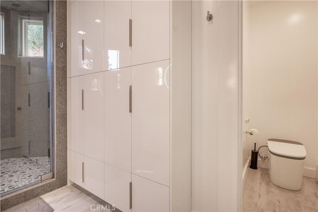 bathroom featuring a shower with door and toilet