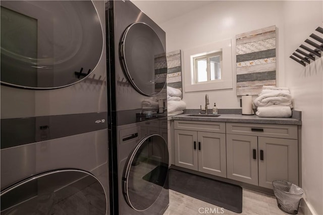 clothes washing area with sink, cabinets, and stacked washer / dryer