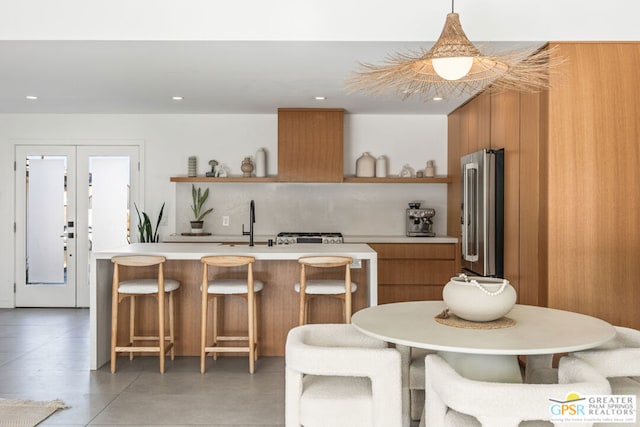 kitchen featuring decorative light fixtures, sink, high end refrigerator, a kitchen island with sink, and french doors