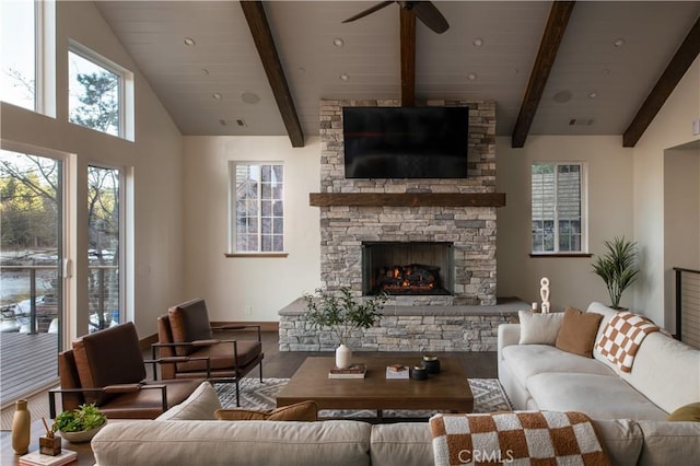 living room with ceiling fan, a stone fireplace, hardwood / wood-style floors, and vaulted ceiling with beams