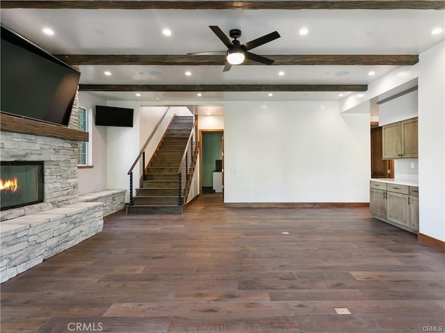 unfurnished living room featuring dark wood-type flooring, ceiling fan, beam ceiling, and a stone fireplace