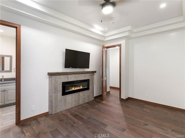 unfurnished living room featuring sink, a tiled fireplace, ceiling fan, a raised ceiling, and dark wood-type flooring