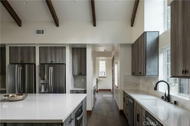 kitchen featuring sink, a center island, beamed ceiling, stainless steel appliances, and backsplash