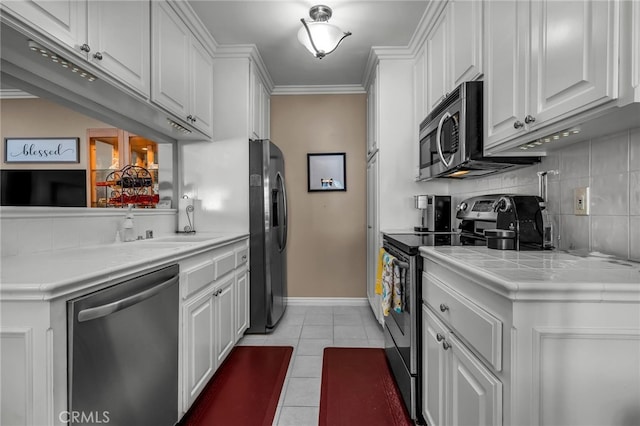 kitchen featuring appliances with stainless steel finishes, white cabinetry, light tile patterned flooring, tile countertops, and kitchen peninsula