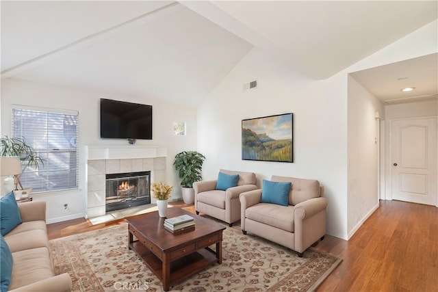 living room with a tiled fireplace, lofted ceiling, wood finished floors, and baseboards