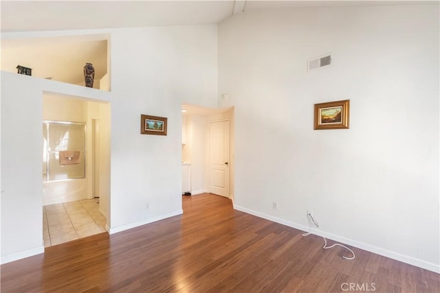 empty room featuring high vaulted ceiling, wood finished floors, visible vents, and baseboards