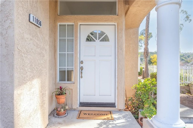 doorway to property featuring stucco siding and fence