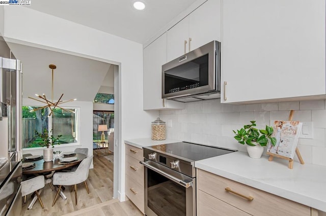 kitchen with white cabinetry, a chandelier, light wood-type flooring, stainless steel appliances, and backsplash