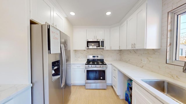 kitchen featuring appliances with stainless steel finishes, white cabinetry, sink, backsplash, and light stone countertops