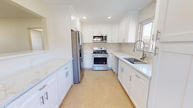 kitchen featuring appliances with stainless steel finishes, white cabinetry, sink, decorative backsplash, and light stone counters