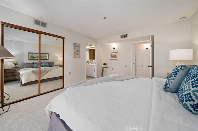 bedroom with ensuite bath, a closet, light carpet, and a textured ceiling