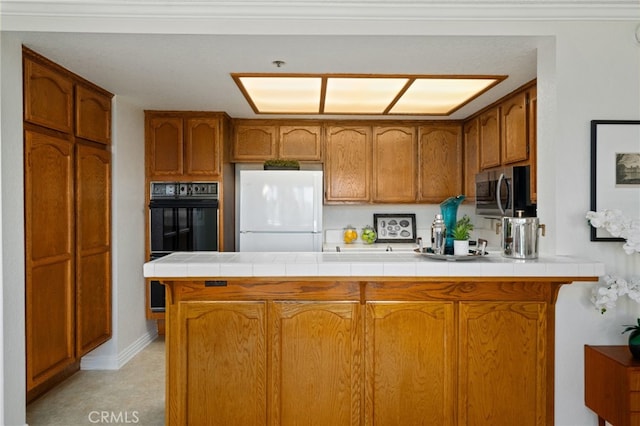 kitchen with white refrigerator, tile counters, double oven, and kitchen peninsula