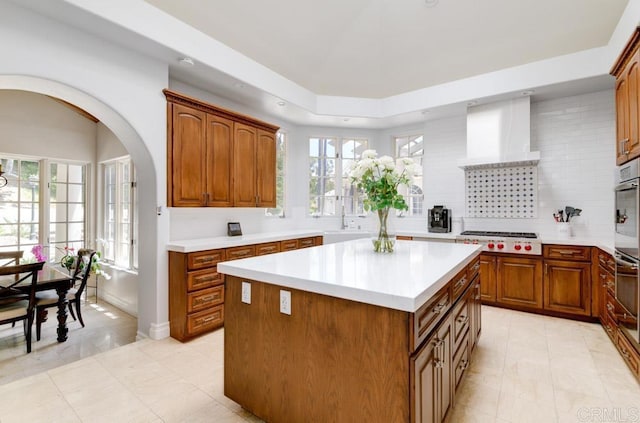 kitchen with sink, wall chimney range hood, a center island, stainless steel gas cooktop, and decorative backsplash