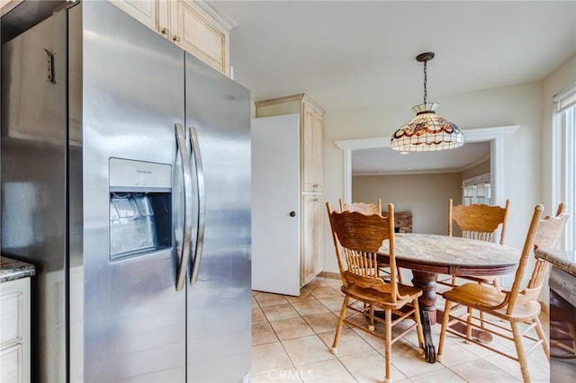 kitchen featuring stainless steel fridge, cream cabinets, hanging light fixtures, and dark stone countertops