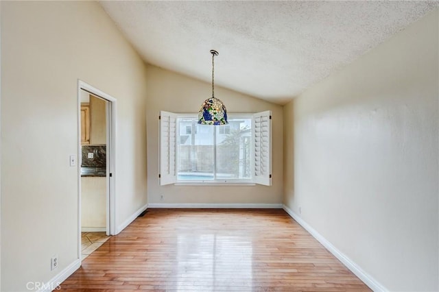 unfurnished dining area featuring vaulted ceiling, light hardwood / wood-style flooring, and a textured ceiling