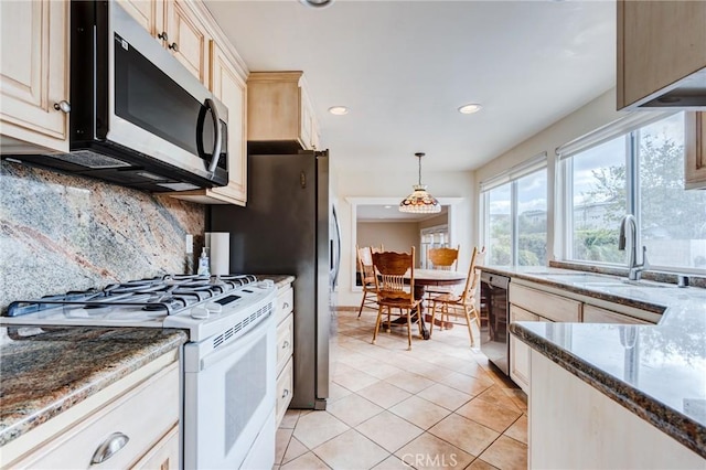 kitchen featuring pendant lighting, sink, decorative backsplash, dark stone counters, and white range with gas stovetop