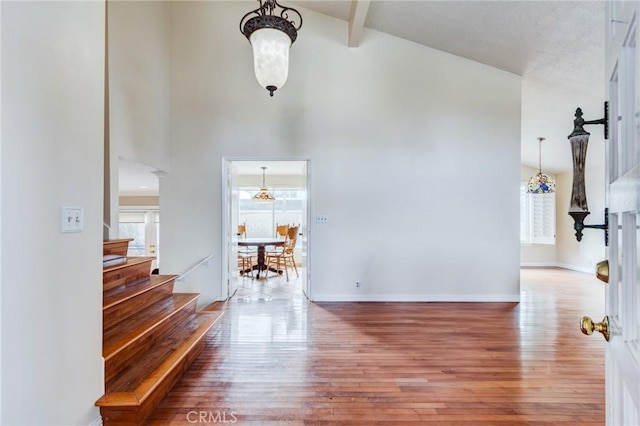 hallway featuring a high ceiling, wood-type flooring, and beam ceiling