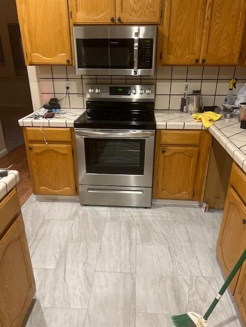 kitchen with tasteful backsplash, appliances with stainless steel finishes, and tile countertops