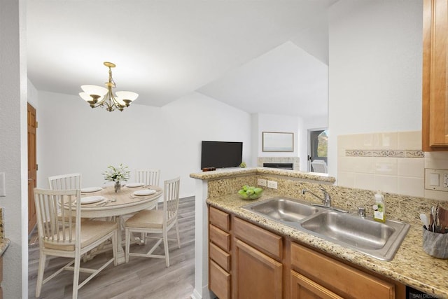 kitchen featuring pendant lighting, sink, a chandelier, light stone countertops, and light wood-type flooring