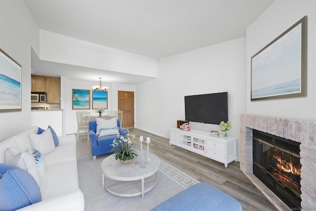 living room with an inviting chandelier, a brick fireplace, and light hardwood / wood-style floors