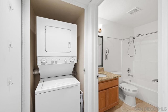 full bathroom featuring stacked washing maching and dryer, vanity, toilet, tub / shower combination, and tile patterned floors