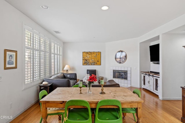 dining area featuring a tile fireplace and light wood-type flooring